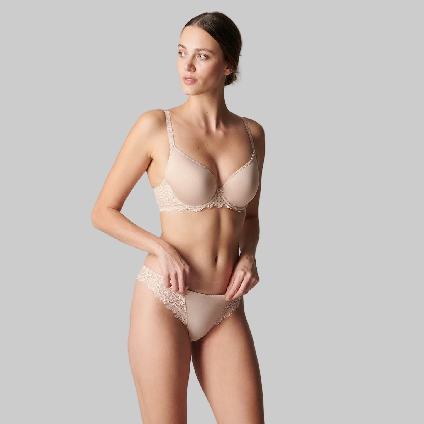 Woman wearing a beige bra and panties set against a plain background