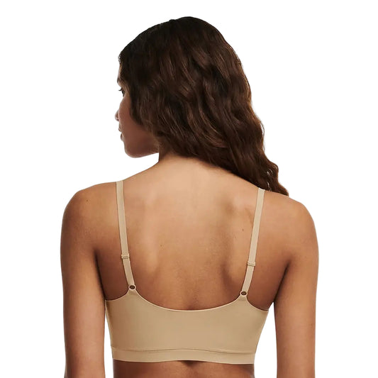 Woman wearing a beige bralette on a plain background