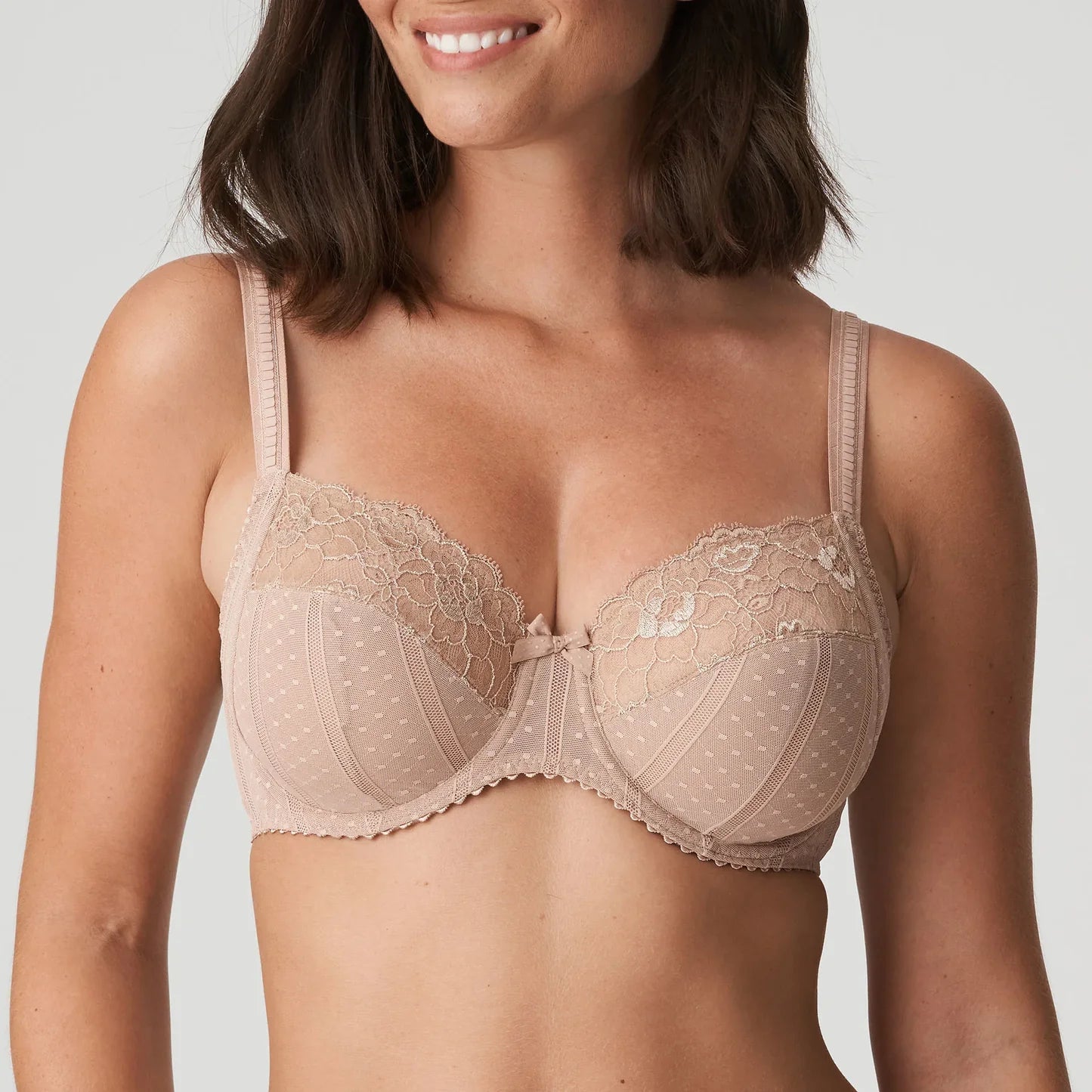 Woman wearing a beige lace bra against a plain background