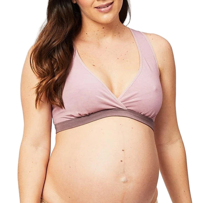 Pregnant woman wearing a pink maternity bra and beige underwear on a light gray background