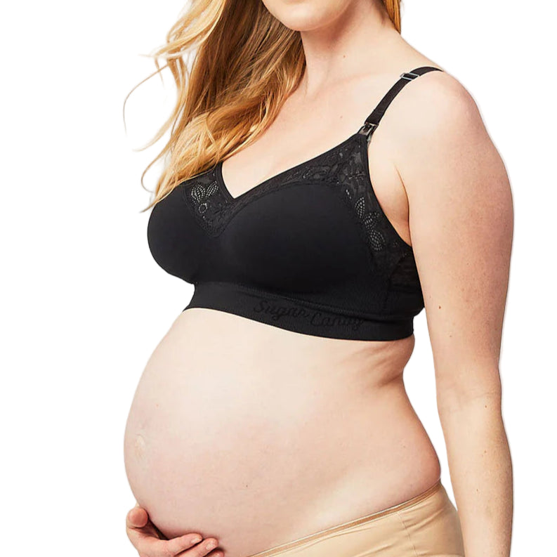 Pregnant woman wearing a black maternity bra and beige underwear on a light gray background