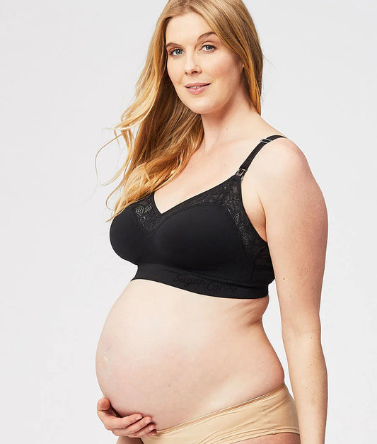 Pregnant woman wearing a black maternity bra and beige underwear on a light gray background