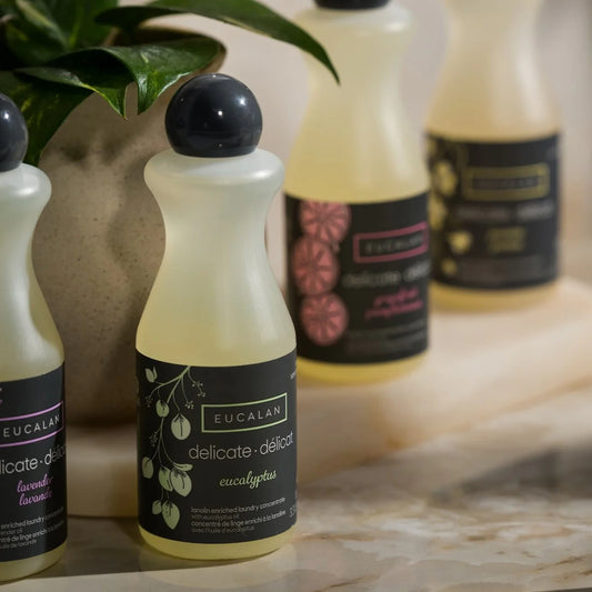 Bottles of Eucalan laundry detergent on a marble surface with a plant in the background.