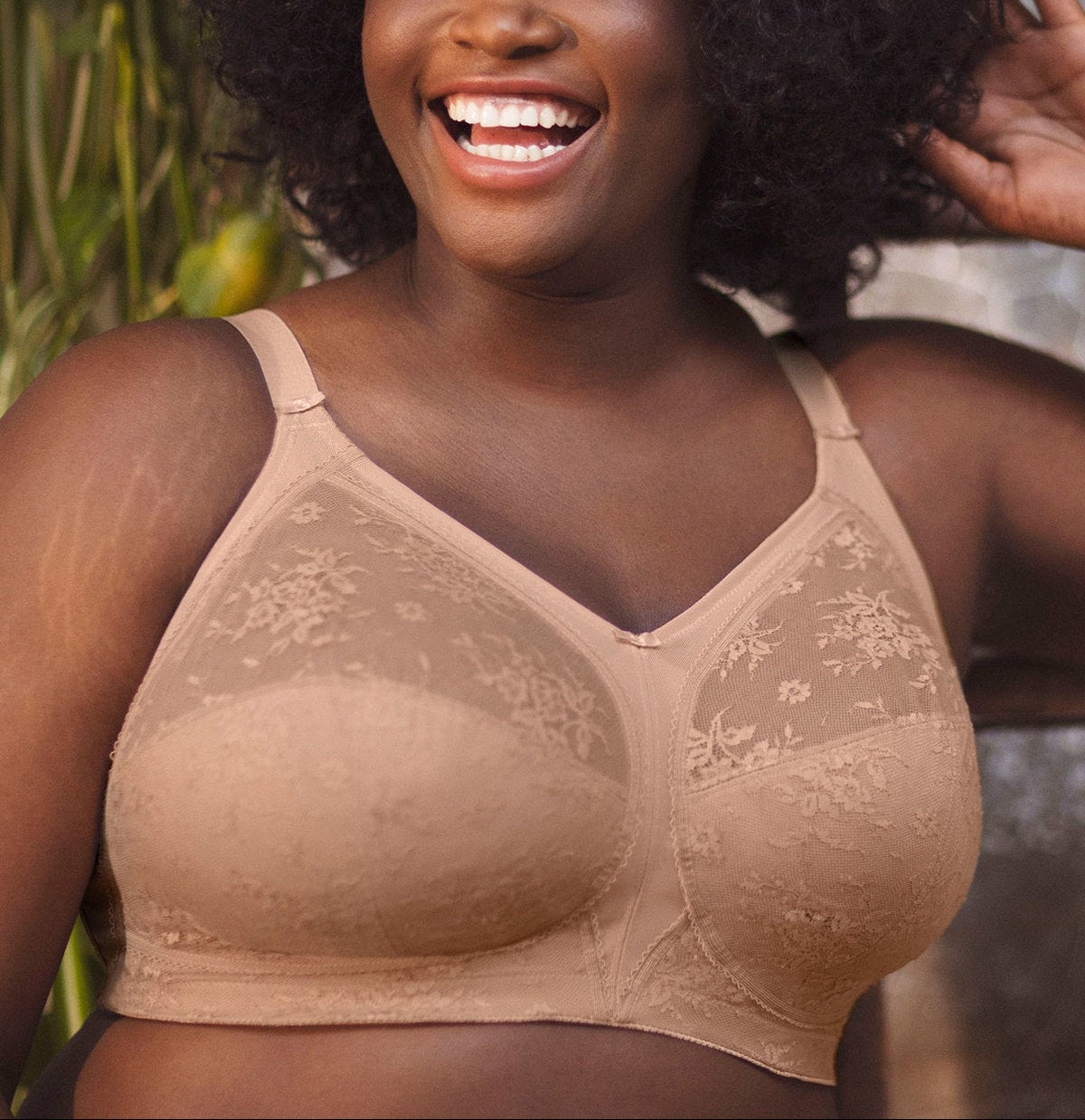 Woman wearing a beige bralette with floral lace details, standing outdoors.